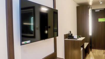 A modern hotel lobby with a large flat-screen TV mounted on a wooden wall, a reception desk, and a wooden floor.
