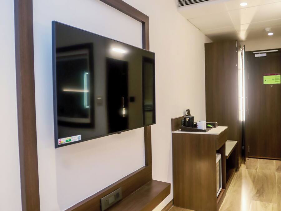 A modern hotel lobby with a large flat-screen TV mounted on a wooden wall, a reception desk, and a wooden floor.