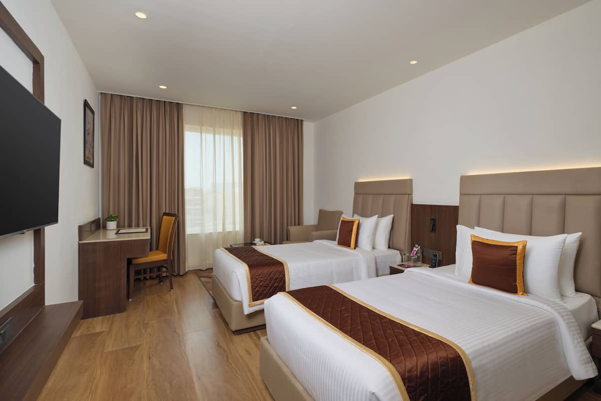 A hotel room with two beds, a desk, a chair, and a television.