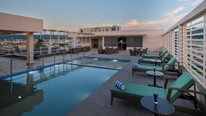 A rooftop pool area with lounge chairs and tables, surrounded by a high wall and overlooking a cityscape. - Regenta Place Gwalior (Gwalior)