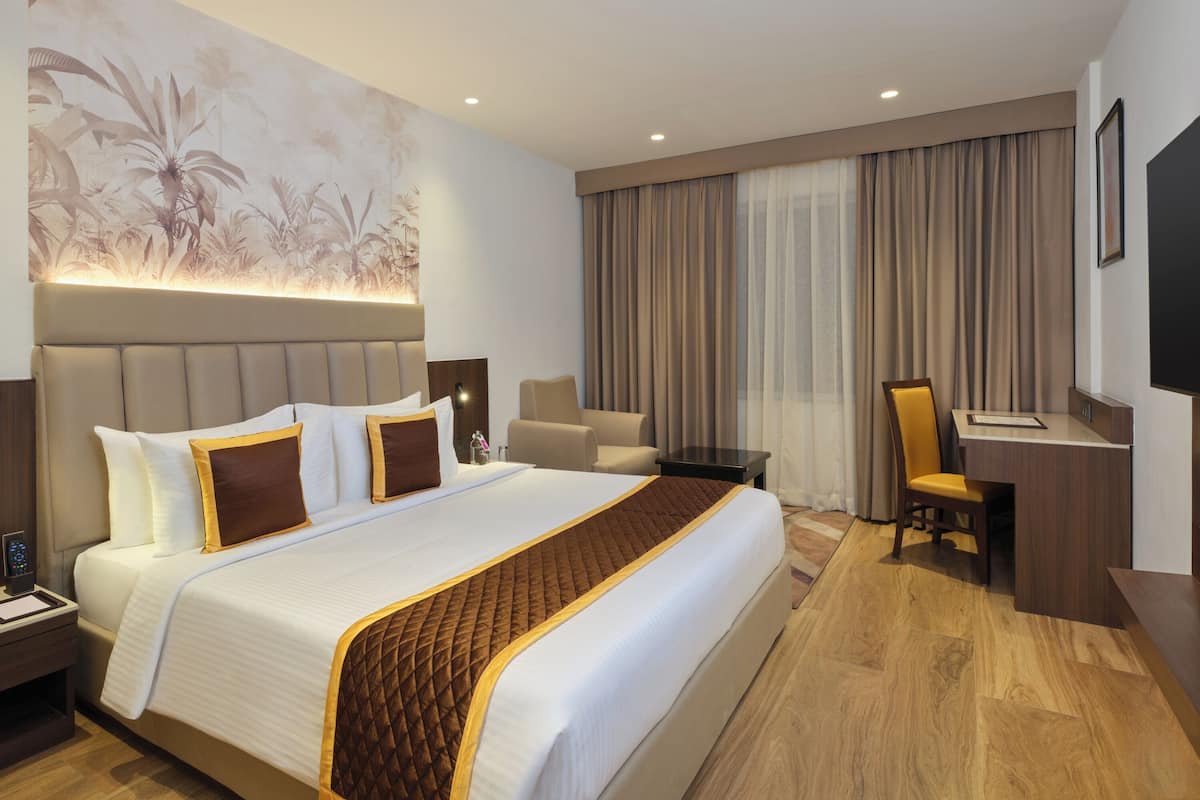 A hotel room with a large bed, a desk, a chair, and a television.