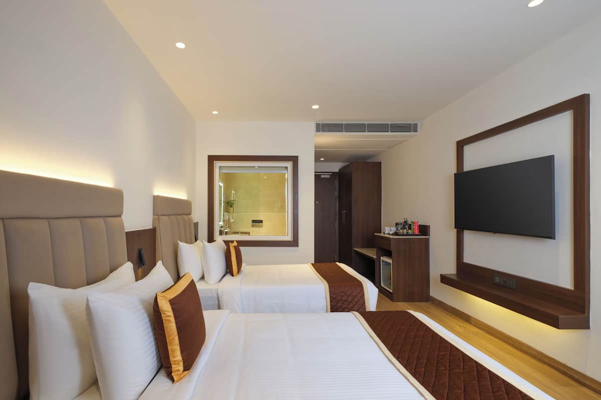 A hotel room with two beds, a TV, and a bathroom visible through a glass door.
