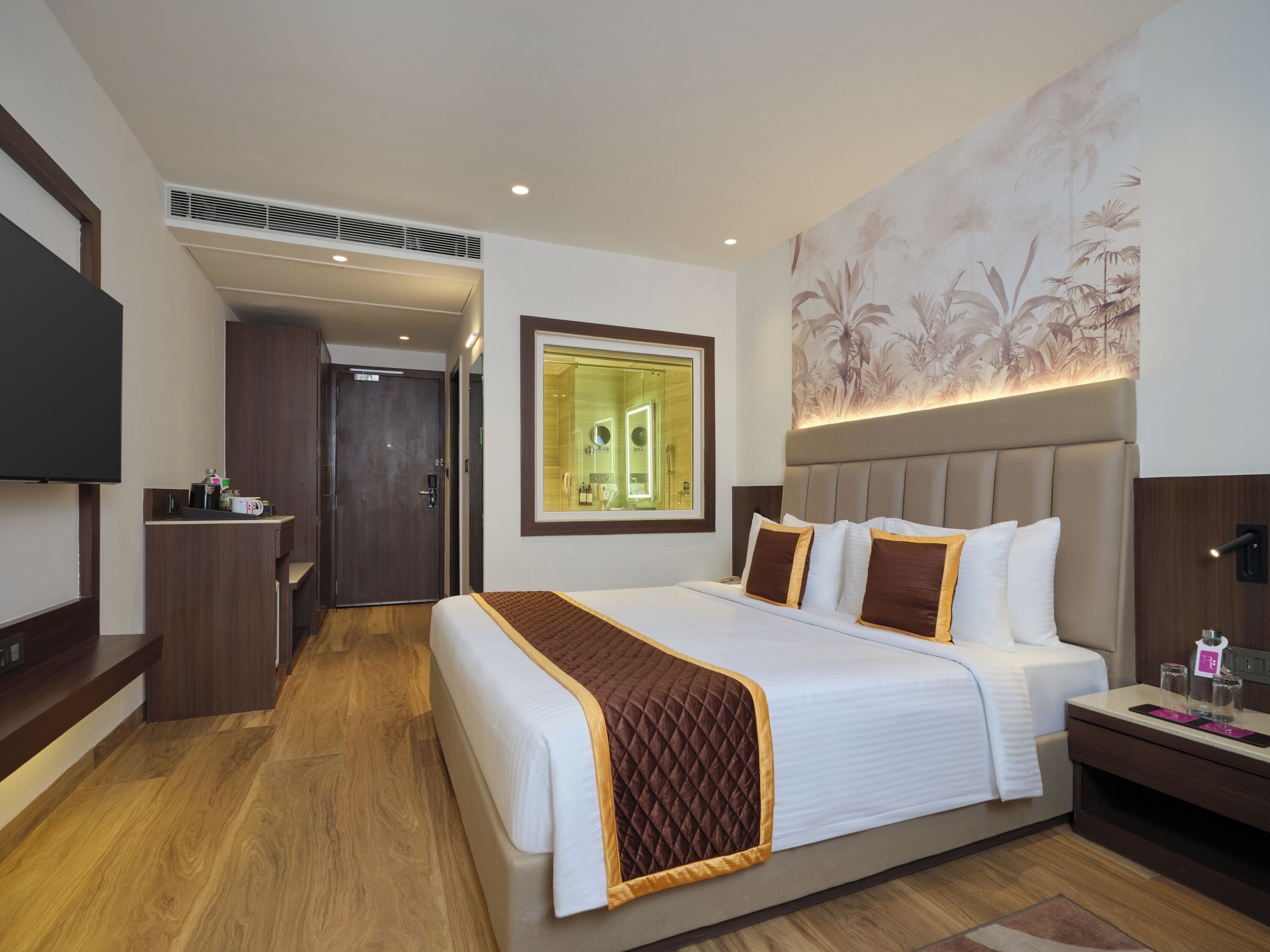 A hotel room with a large bed, a TV, a desk, and a bathroom with a mirror.