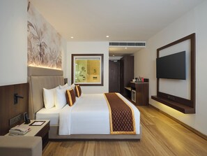 Habitación de hotel con una cama grande, un televisor montado en la pared, un escritorio con teléfono y un baño visible a través de una puerta de vidrio.