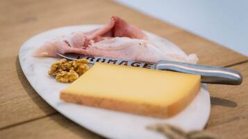 A plate with a slice of cheese, a piece of ham, and walnuts on a wooden table.