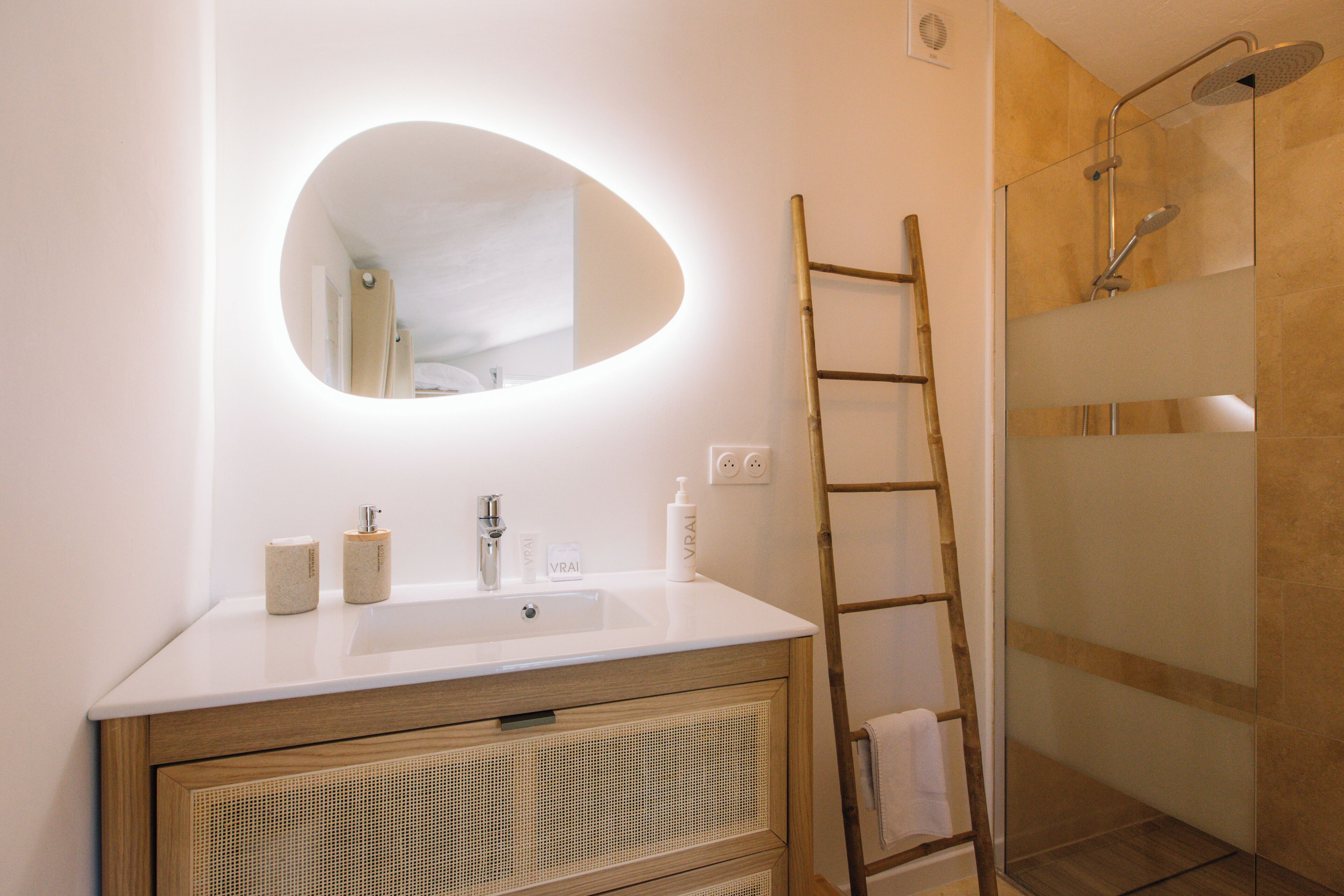 A bathroom with a white sink, mirror, and shower. There is a wooden ladder leaning against the wall.