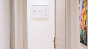Un couloir avec une porte donnant sur une pièce, un tableau encadré au mur et une œuvre d’art colorée sur le côté droit.