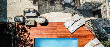 An aerial view of a swimming pool area with lounge chairs, a wooden deck, and stone walls.