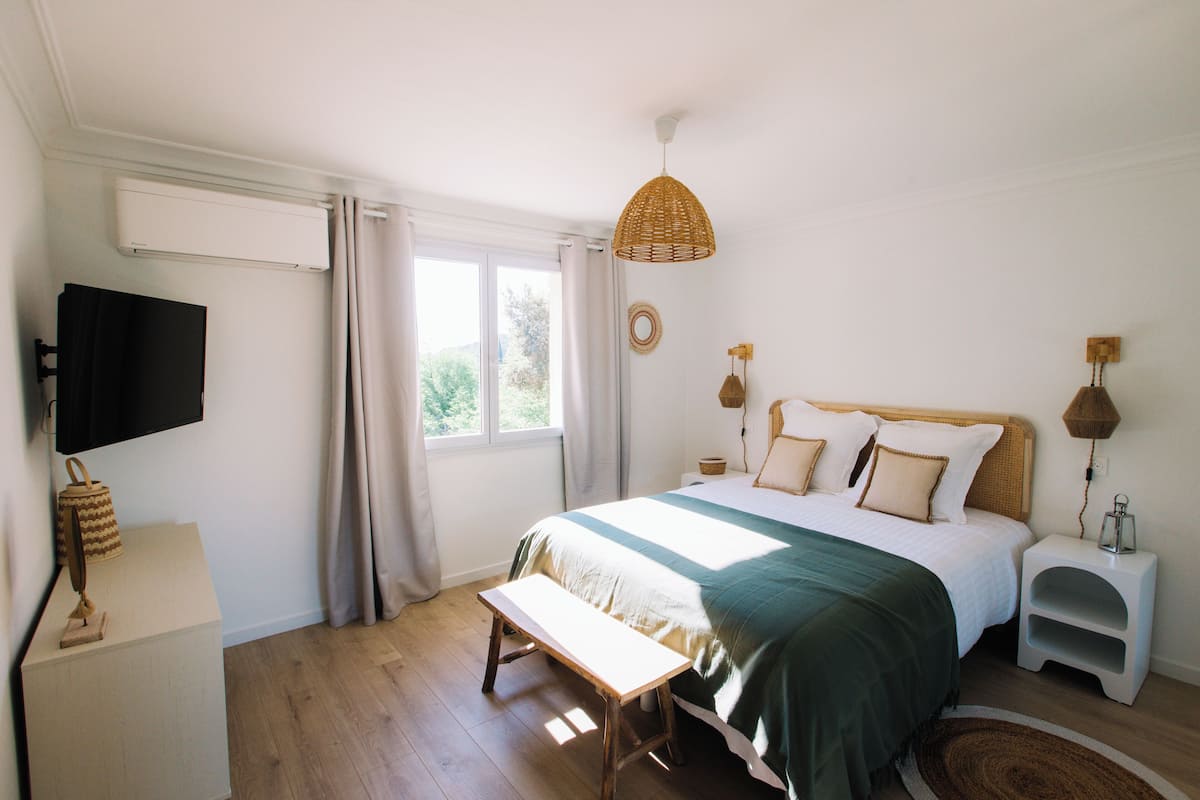 A bedroom with a bed, bedside tables, a bench, a television, and a window with curtains.
