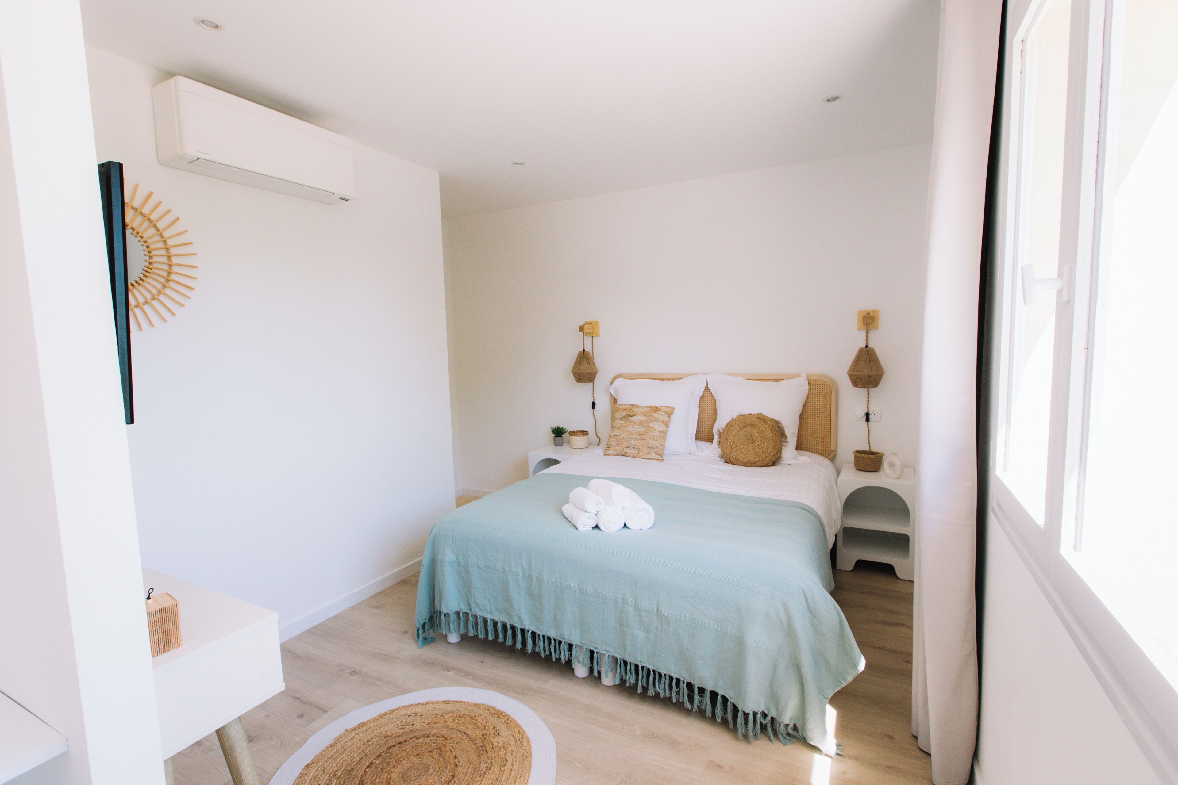 Un dormitorio con cama, mesitas de noche, aire acondicionado de pared y una ventana.