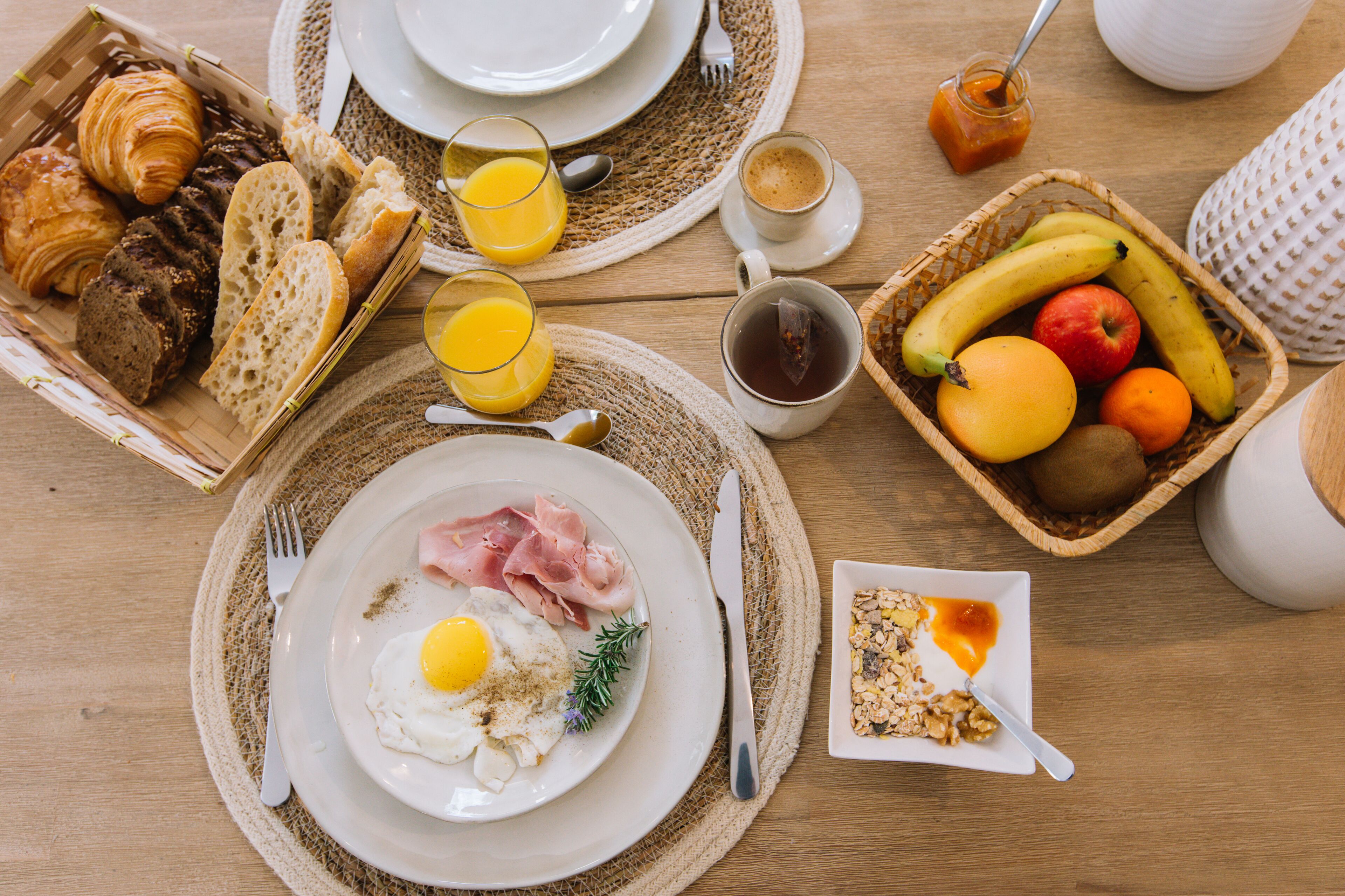 A breakfast setting with croissants, bread, eggs, ham, and a fruit bowl.