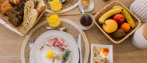 A breakfast setting with croissants, bread, eggs, ham, and a fruit bowl.