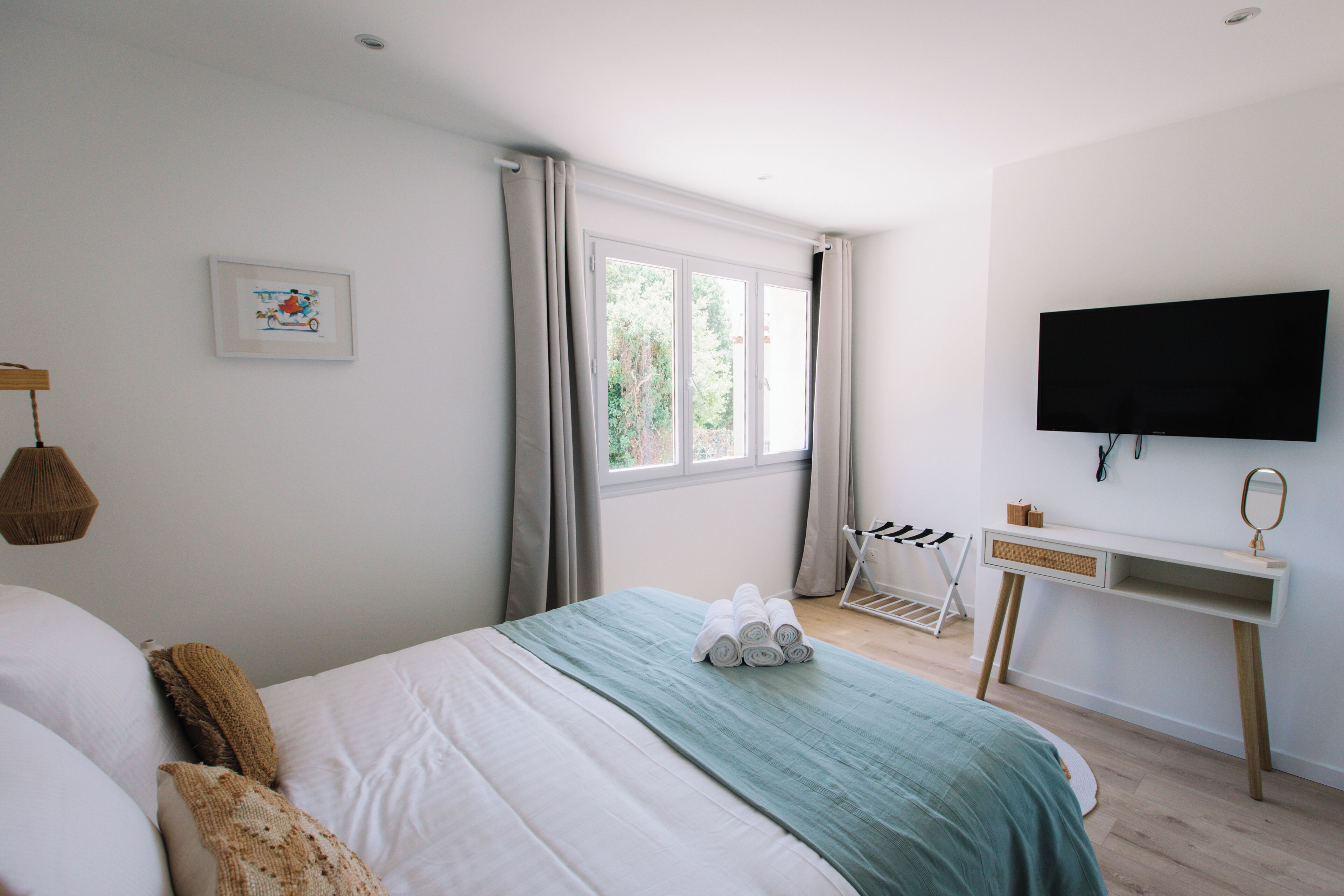 A bedroom with a bed, a desk, a TV, and a window with curtains.