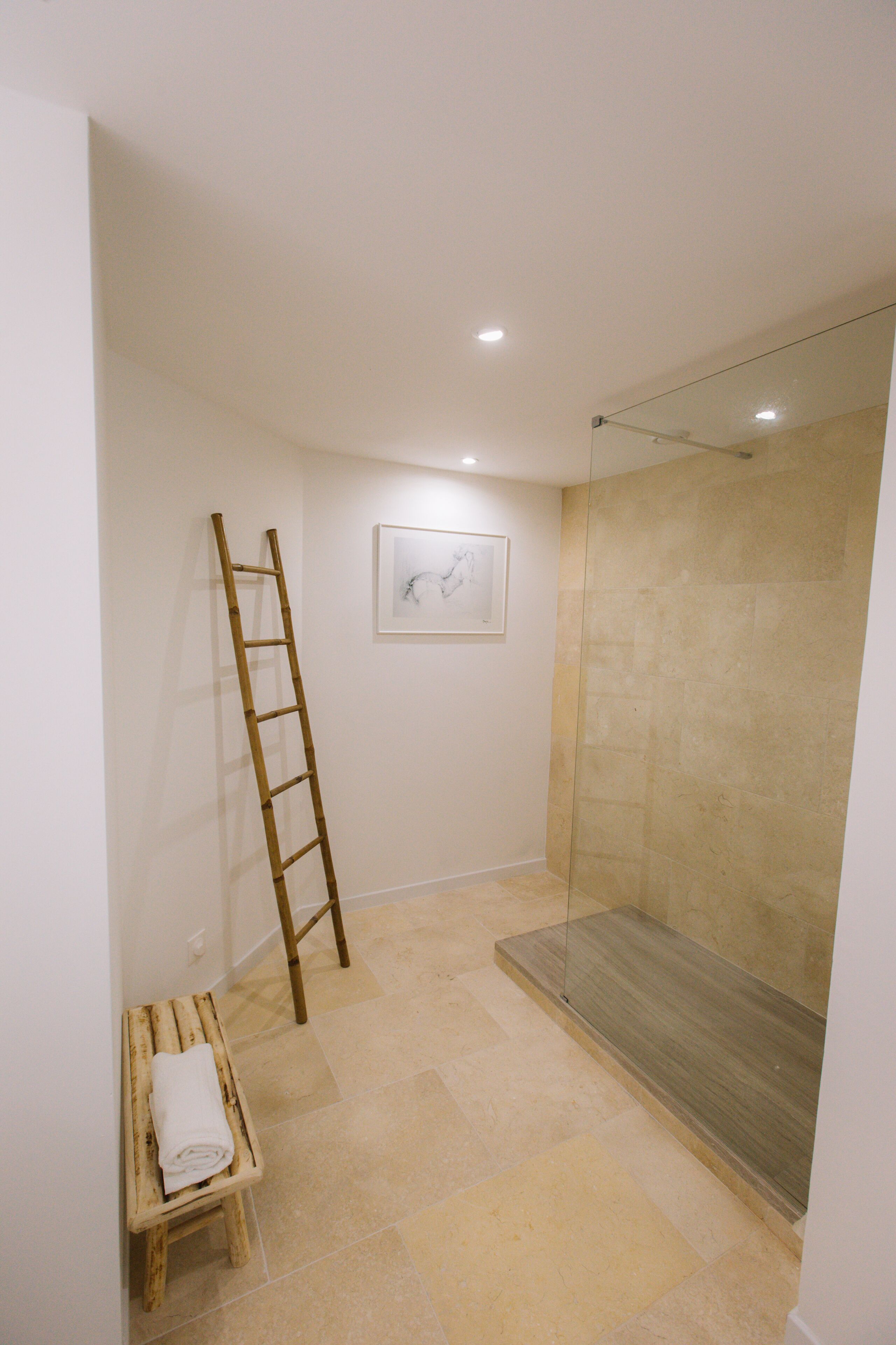 Un baño con ducha, una escalera de madera y un pequeño banco con una toalla.