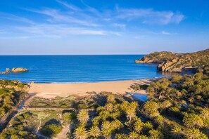 Un paisaje costero con playa arenosa, afloramientos rocosos y vegetación densa.