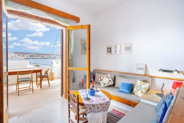 Una habitación acogedora con una mesa y sillas de madera, un sofá con cojines coloridos y vistas a la ciudad a través de un ventanal grande.