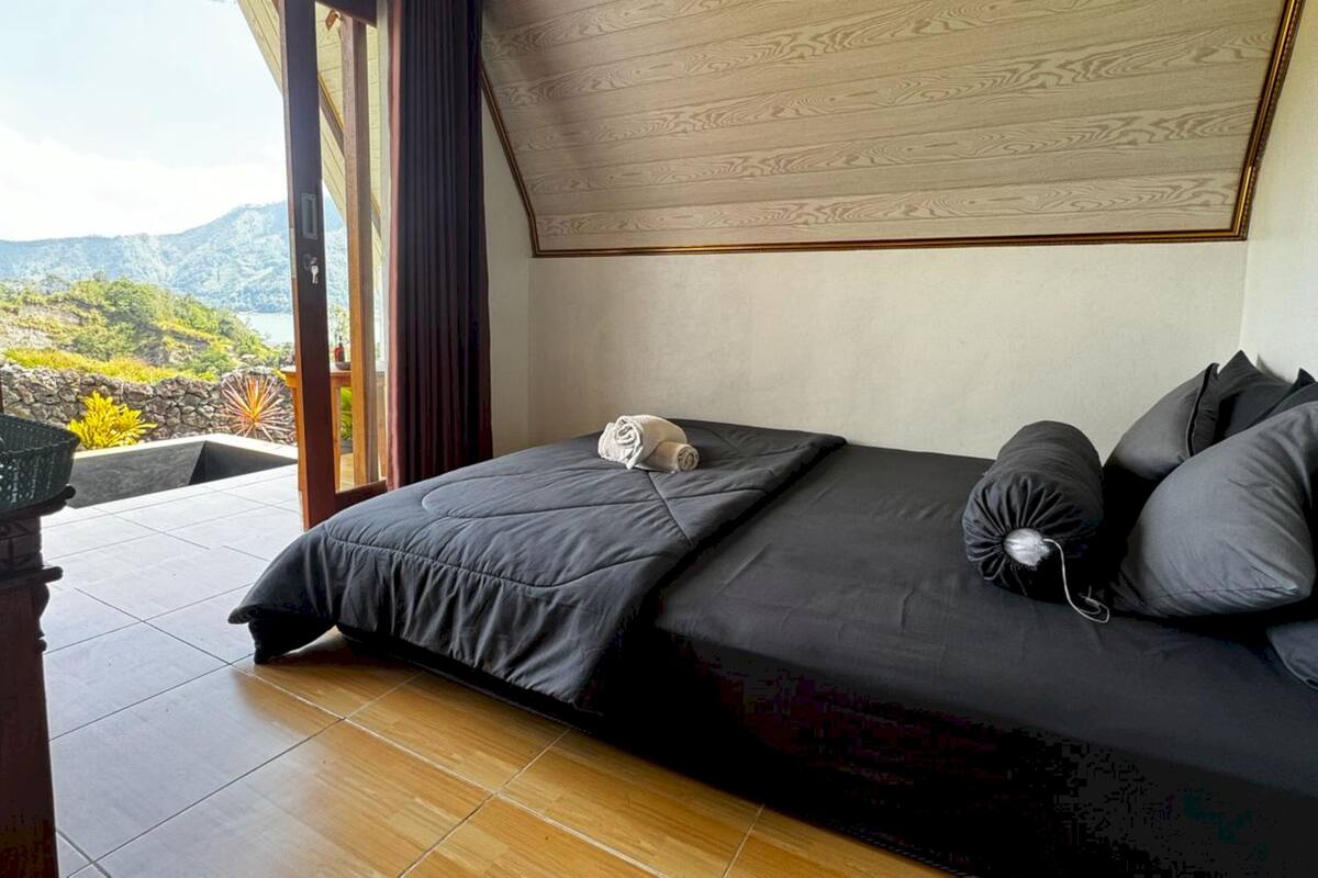 A bedroom with a bed, a view of the outdoors, and a wooden floor.
