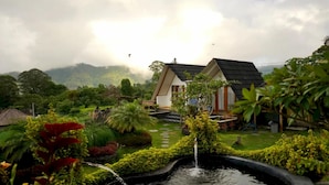 Une maison avec un jardin, un étang et une montagne en arrière-plan.