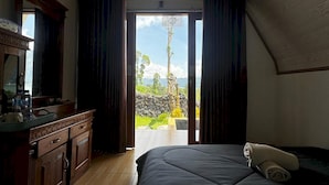 Une chambre avec un lit, une commode et une vue sur un paysage tropical, visible à travers une porte ouverte.
