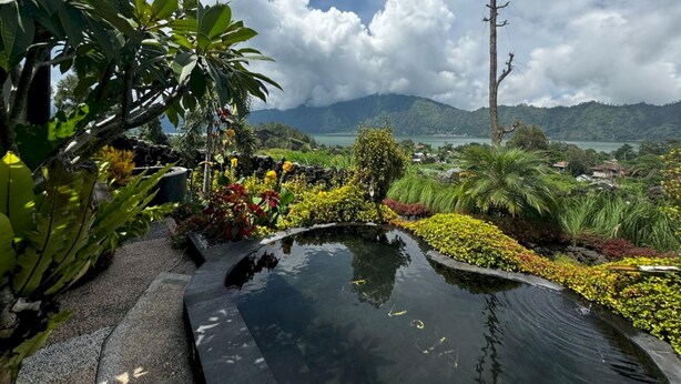 Un jardin aménagé avec un étang, des plantes tropicales et une vue sur les montagnes lointaines.