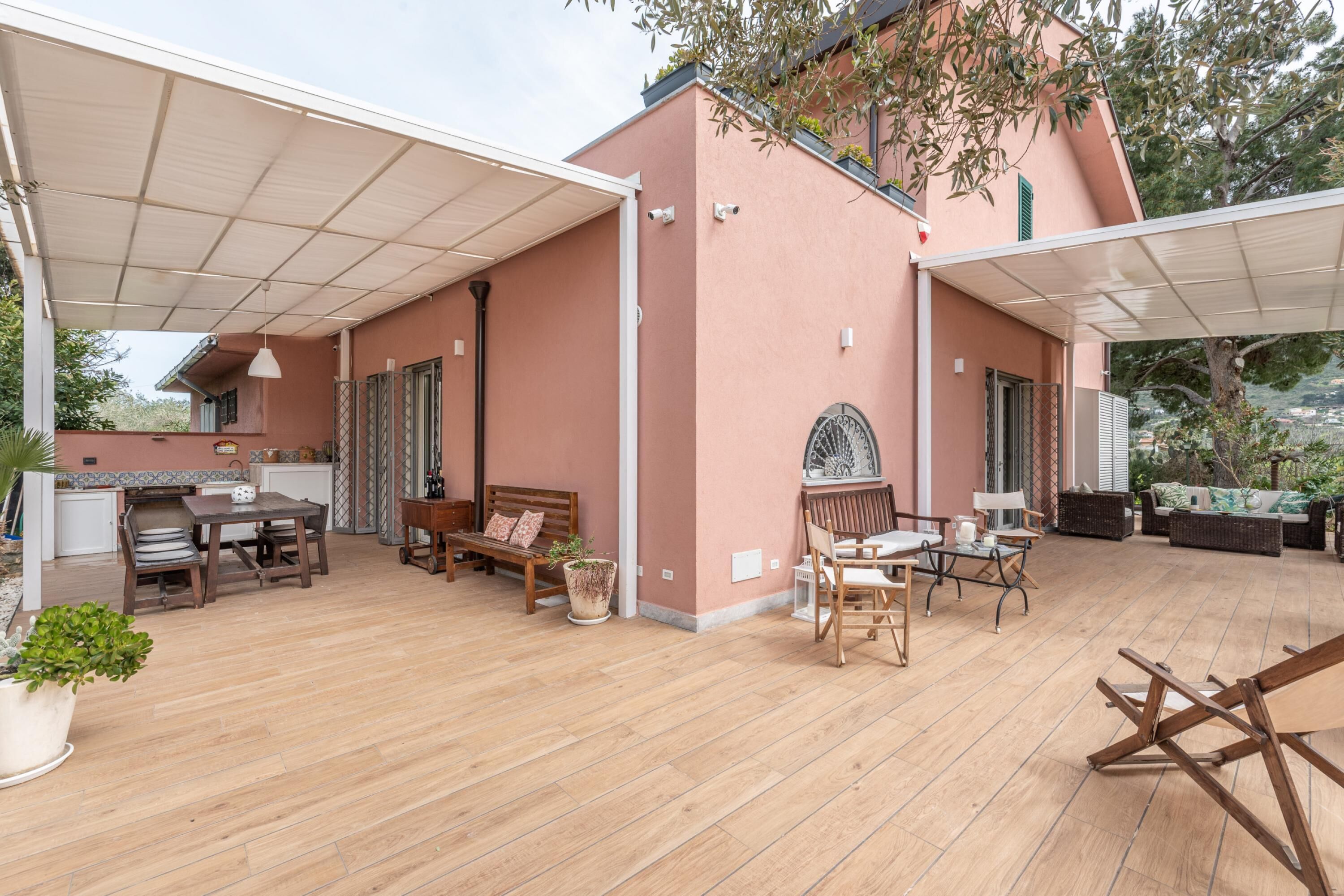 Un patio couvert doté d’un plancher en bois, une table à manger avec des chaises, un canapé et un petit coin salon avec un banc et des coussins.