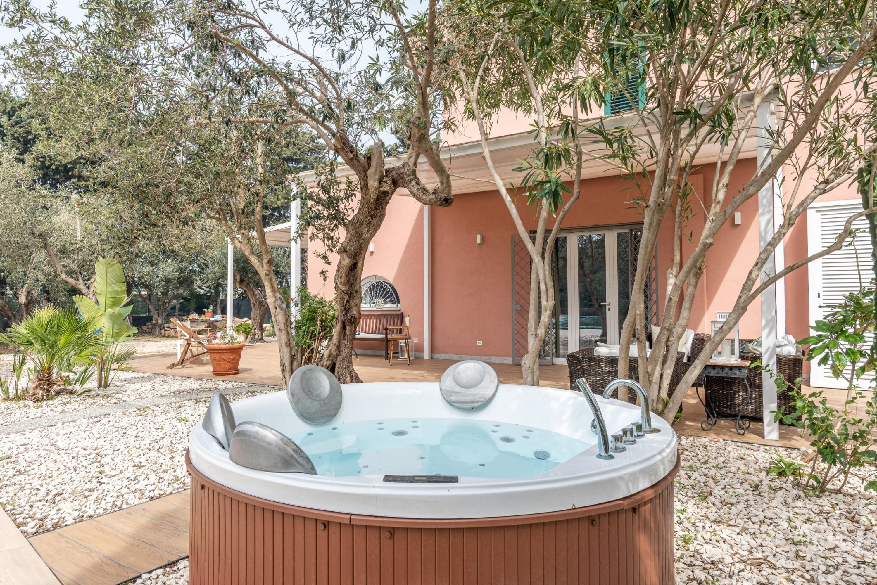 A hot tub in a garden area with trees and outdoor furniture.