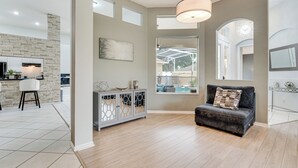 A spacious living area with a grey sofa, a white cabinet with glass doors, and a stone accent wall. - Game Room, Pool & Spa: Disney Area Getaway! (Haines City)