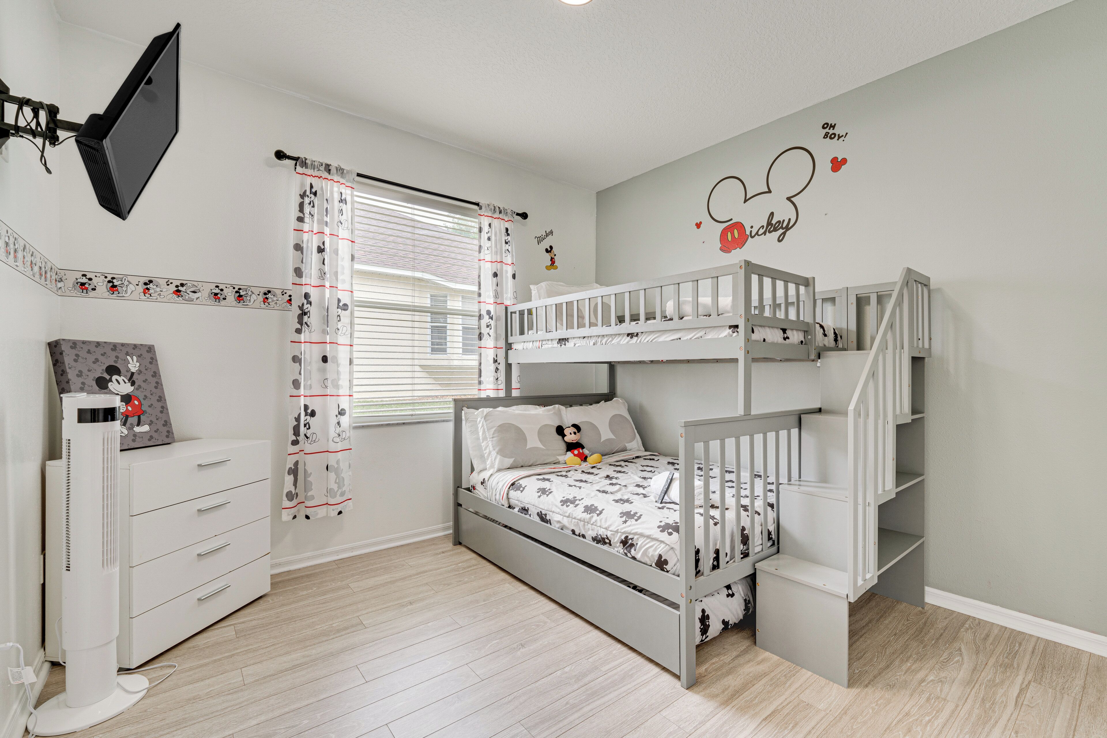 A child's bedroom with a bunk bed, a dresser, a flat-screen TV, and Mickey Mouse wall decals.