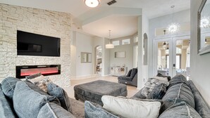 A modern living room with a stone wall, a flat-screen TV, and a gray sectional sofa. - Game Room, Pool & Spa: Disney Area Getaway! (Haines City)