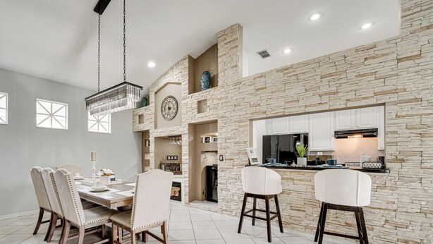 A spacious dining area with a high ceiling, stone wall, and modern kitchen with white cabinets and a large window. - Game Room, Pool & Spa: Disney Area Getaway! (Haines City)