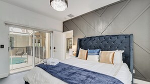 A modern bedroom with a large bed, a chandelier, and a view of a swimming pool through glass doors. - Game Room, Pool & Spa: Disney Area Getaway! (Haines City)