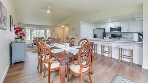 A spacious dining area with a wooden table and chairs, a kitchen with white cabinets and a stainless steel refrigerator, and a ceiling fan.