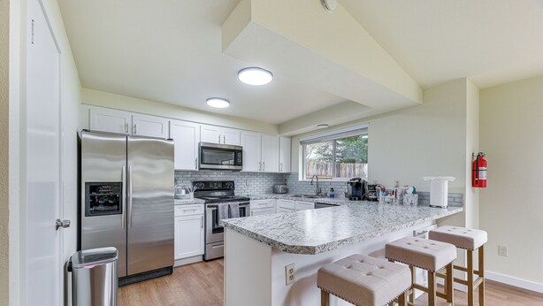 A modern kitchen with stainless steel appliances, white cabinetry, a marble countertop, and a built-in island with bar stools.
