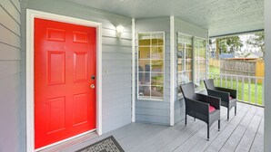 A porch with a red door, wicker chairs, and a view of a backyard.
