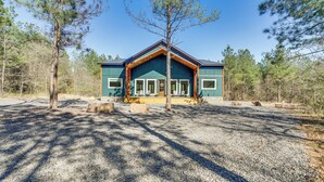 A cabin with a large porch, surrounded by trees and a gravel driveway. - Broken Bow Cabin ~ 5 Mi to State Park w/ Hot Tub! (Broken Bow)