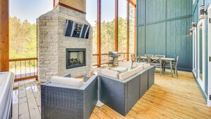 A covered outdoor area with stone fireplace, wicker furniture, and a wooden deck. - Broken Bow Cabin ~ 5 Mi to State Park w/ Hot Tub! (Broken Bow)