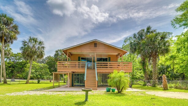 Una casa de madera de dos pisos con un balcón, rodeada de exuberante vegetación y palmeras.