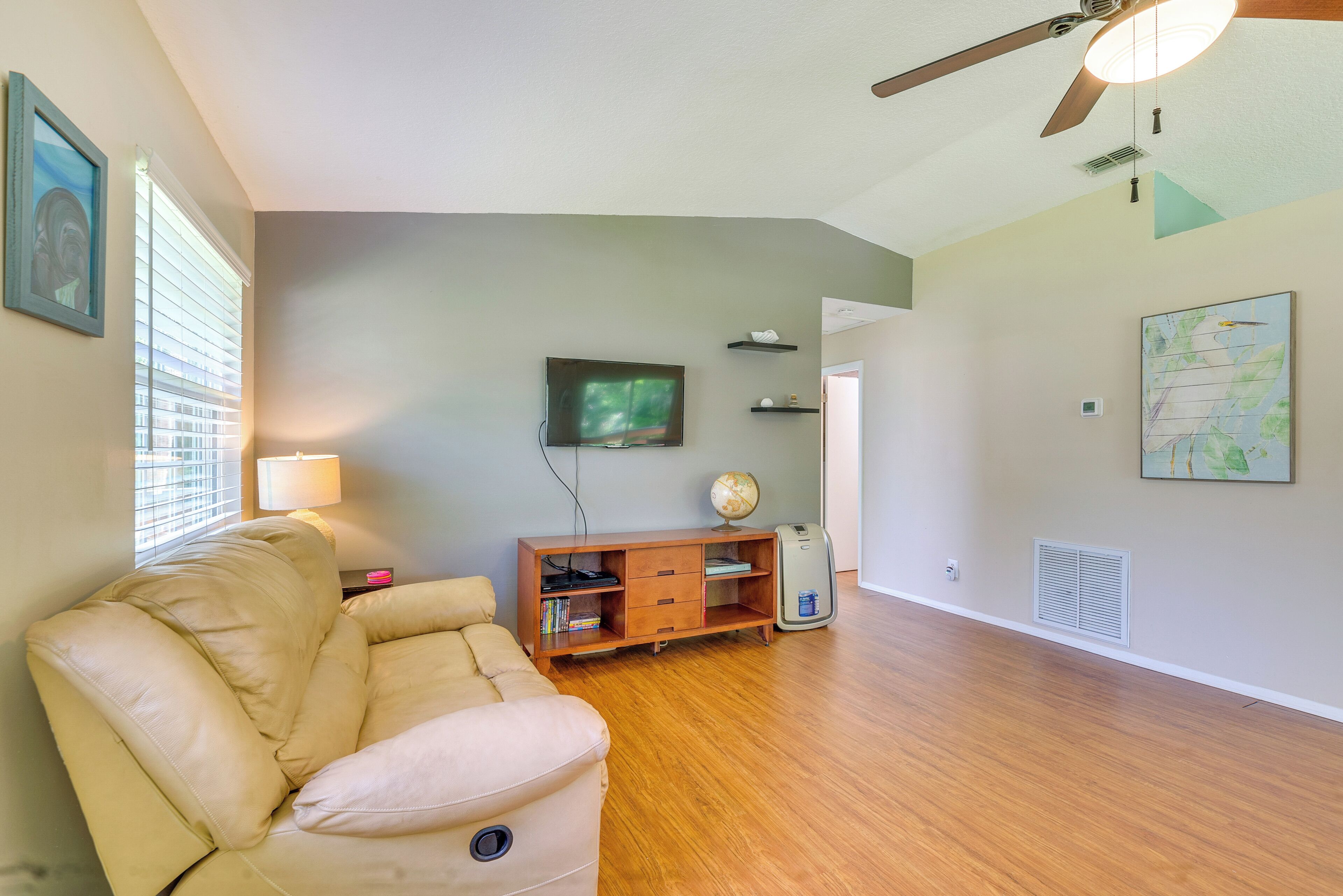 Una sala de estar con sofá color beige, centro de entretenimiento de madera y ventilador de techo.
