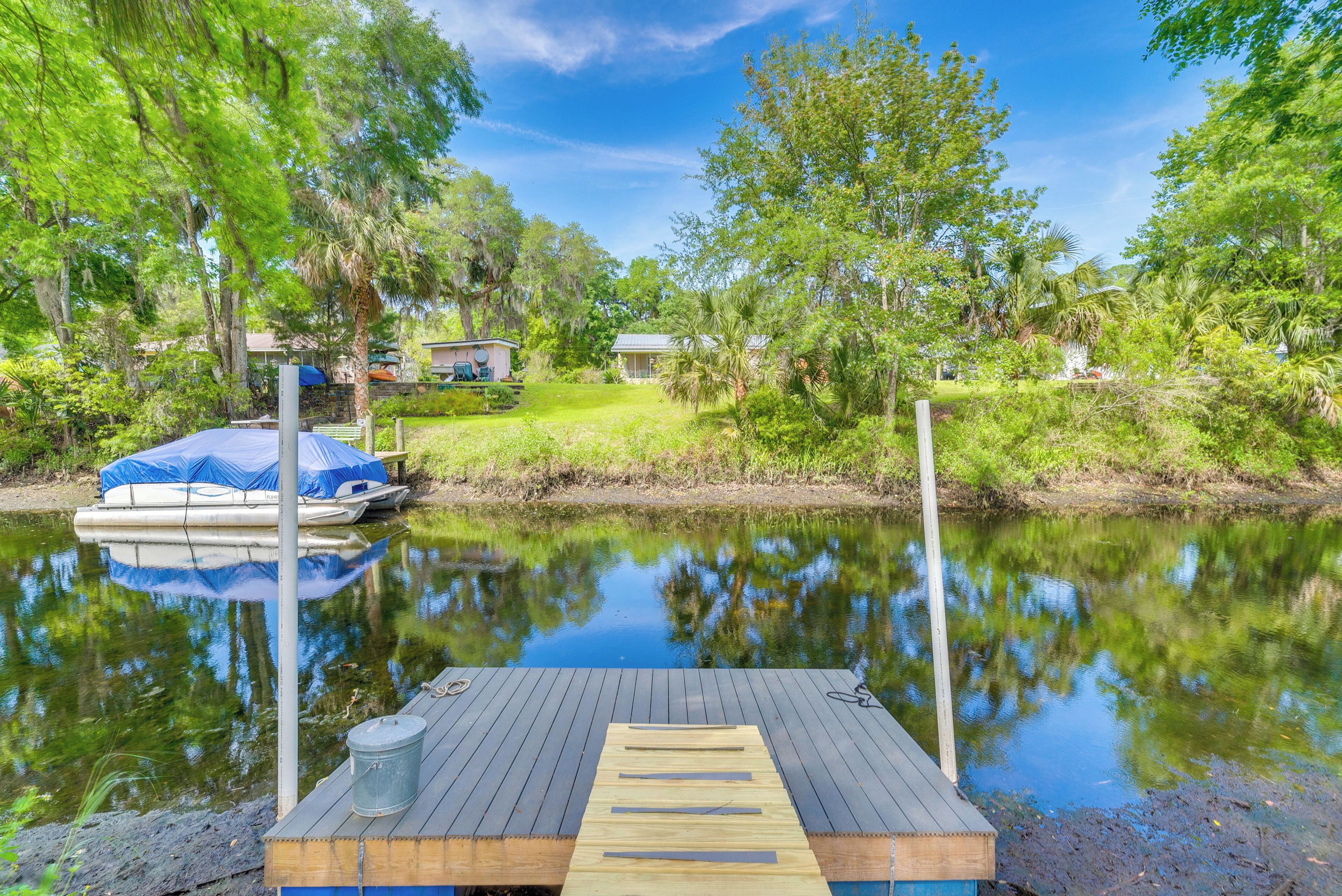 A wooden dock extending into a calm river, surrounded by lush greenery and trees.