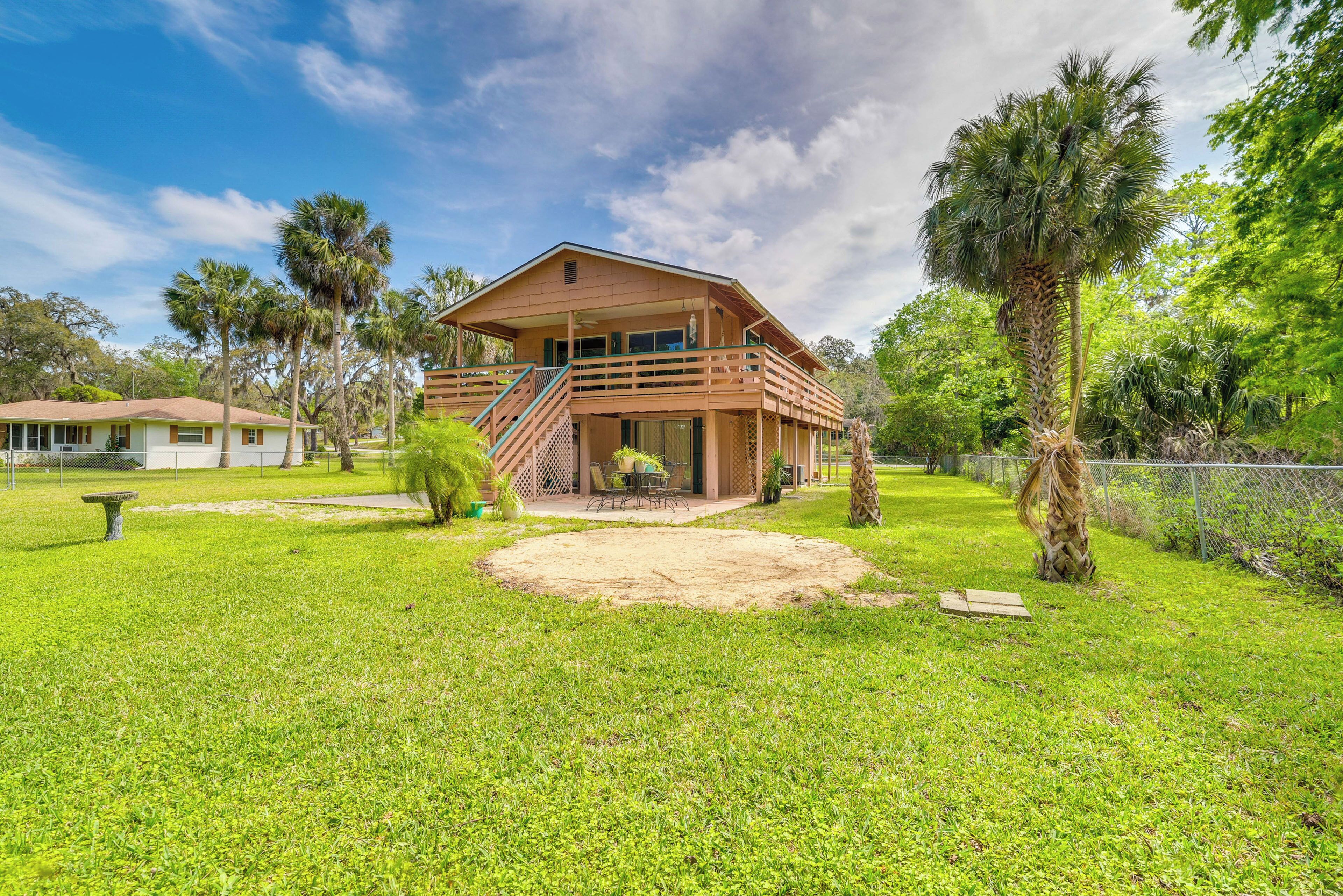A two-story wooden house with a balcony, surrounded by lush greenery and a well-maintained lawn.