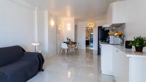 A modern living room with a sofa, a dining table with chairs, a kitchen area with a refrigerator, and a potted plant. - Cap Ferrat View III AP4401 By Riviera Holiday Hom (Saint-Jean-Cap-Ferrat)