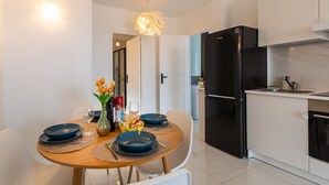 A modern kitchen with a black refrigerator, white cabinets, and a dining area with a wooden table set for two. - Cap Ferrat View III AP4401 By Riviera Holiday Hom (Saint-Jean-Cap-Ferrat)