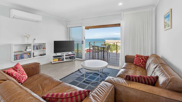 Un salon moderne avec un canapé en cuir, un téléviseur à écran plat, une bibliothèque et un balcon offrant une vue sur la mer.
