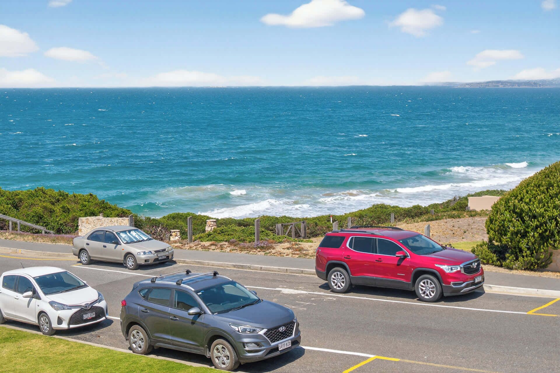 Un parking où sont garées des voitures, le long d’une route côtière offrant une vue sur l’océan.