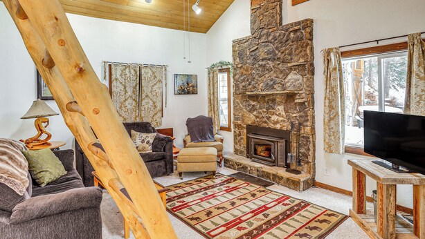Un salón acogedor con chimenea de piedra, vigas de madera en el techo y un televisor sobre un mueble de madera.