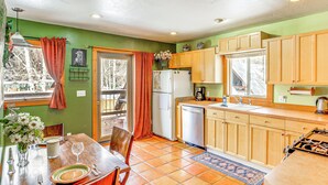 Una cocina con armarios de madera, un refrigerador, un lavamanos y un comedor con mesa y sillas.