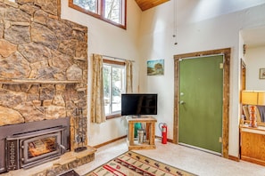 A stone fireplace, a television, a green door, and a fire extinguisher in a living room.