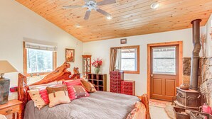 Un dormitorio acogedor con techo de madera, una cama grande con muchas almohadas, un aparador, una ventana y un estufa de leña.