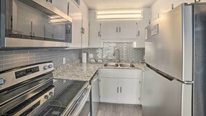 A modern kitchen with white cabinets, a stainless steel refrigerator, a built-in oven, and a granite countertop. - Oceanfront Panama City Beach Condo w/ Pool Access (Panama City Beach)