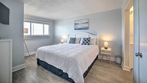 A bedroom with a large bed, two bedside tables with lamps, a window with blinds, and a painting on the wall. - Oceanfront Panama City Beach Condo w/ Pool Access (Panama City Beach)